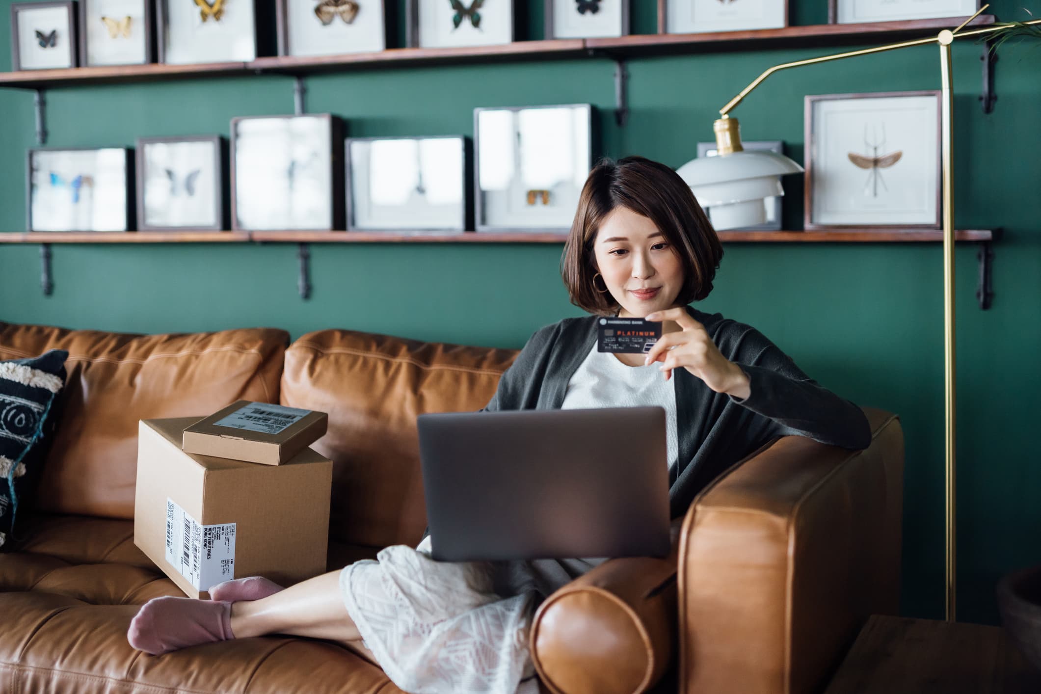 A woman on her sofa in the evening, laptop open and card in hand, checking out online.